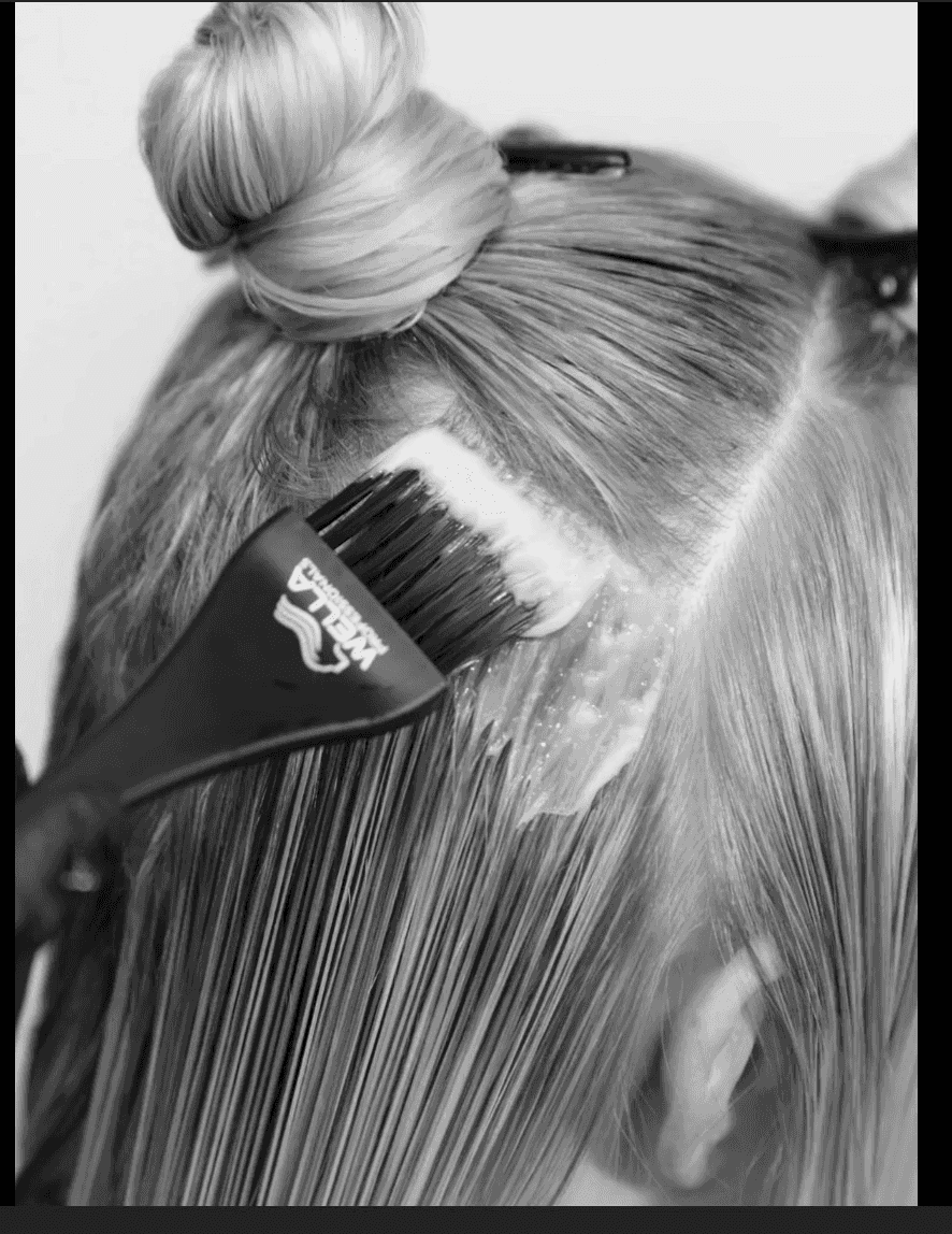 Hair being dyed with a brush, sectioned into neat parts, showcasing the coloring process.