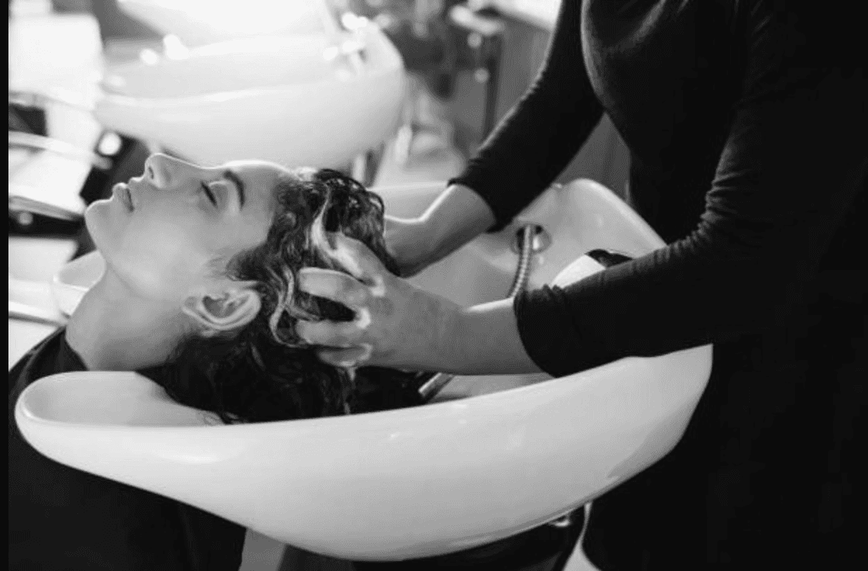 Hairdresser washing woman's hair at salon sink.