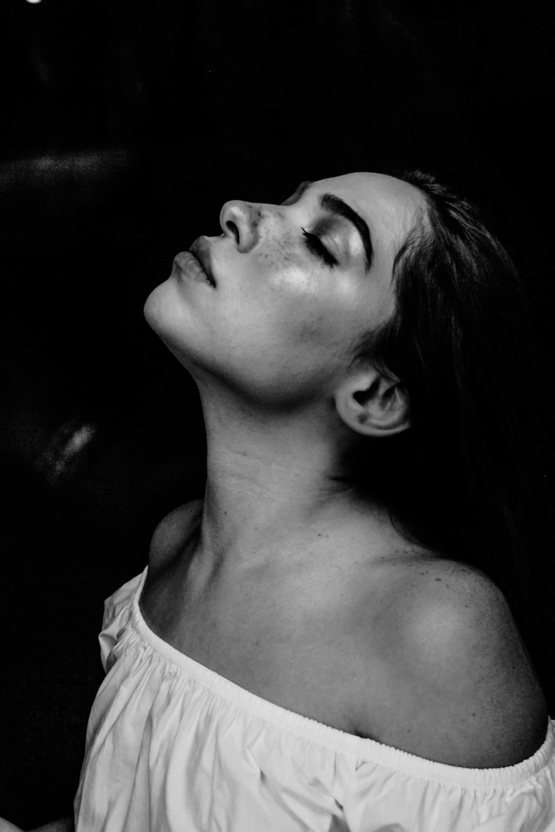 Woman in profile with eyes closed, head tilted back, wearing an off-the-shoulder top.
