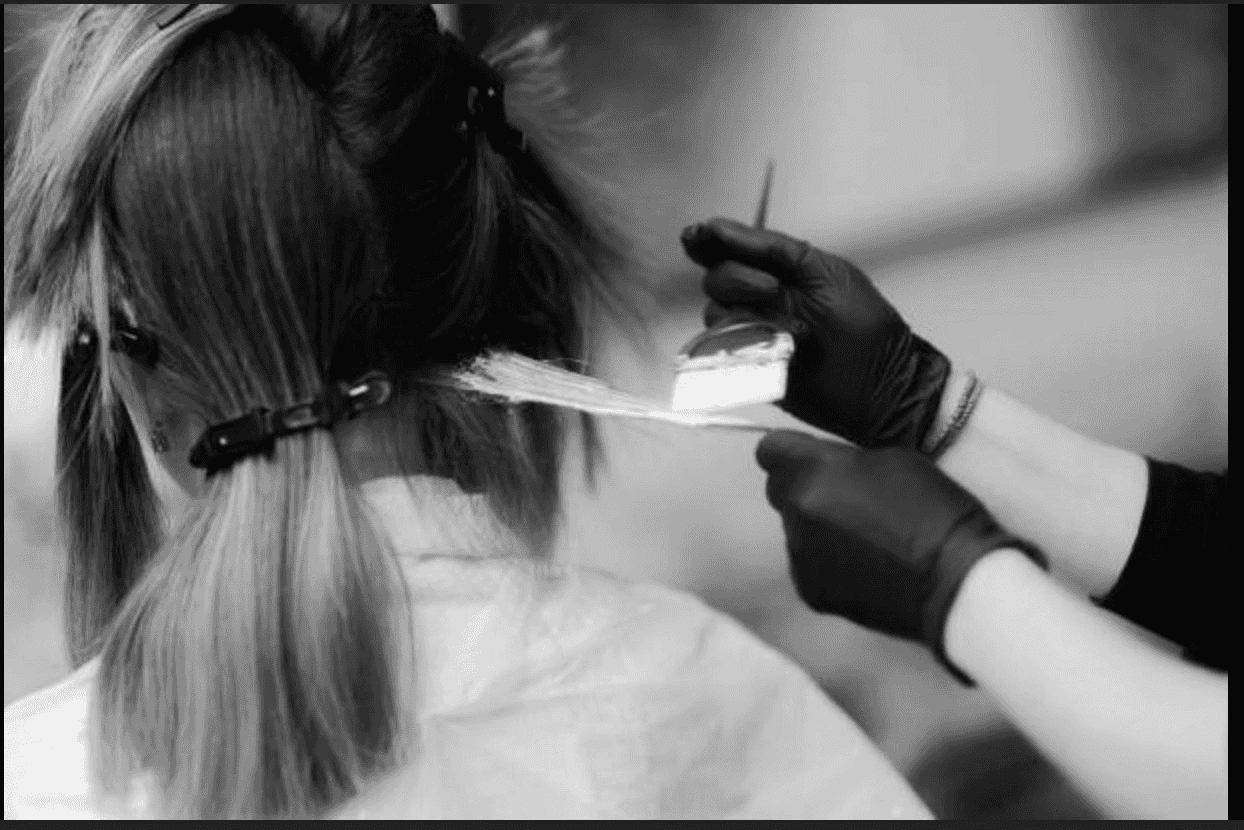 Hairdresser applying dye to a client's hair with a brush in a salon.