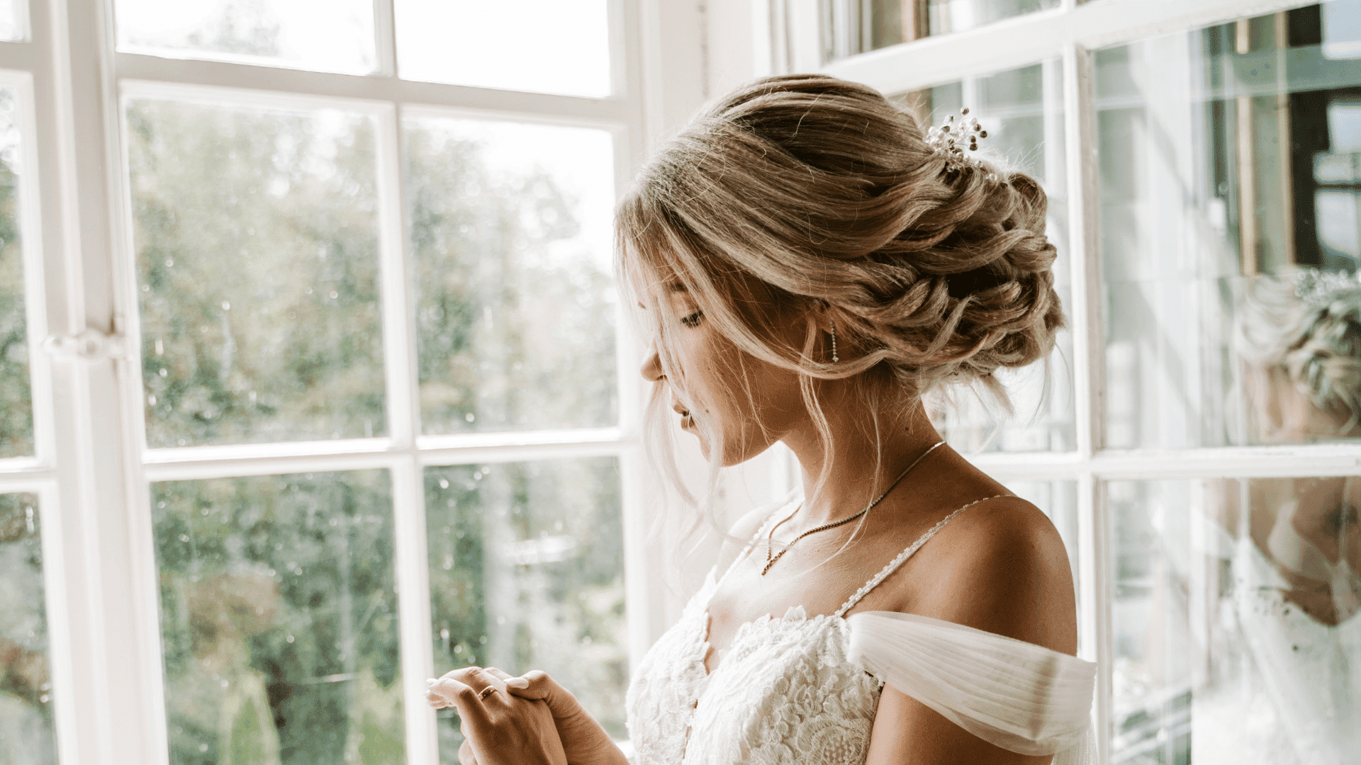 Bride in elegant dress gazes at ring near bright window.