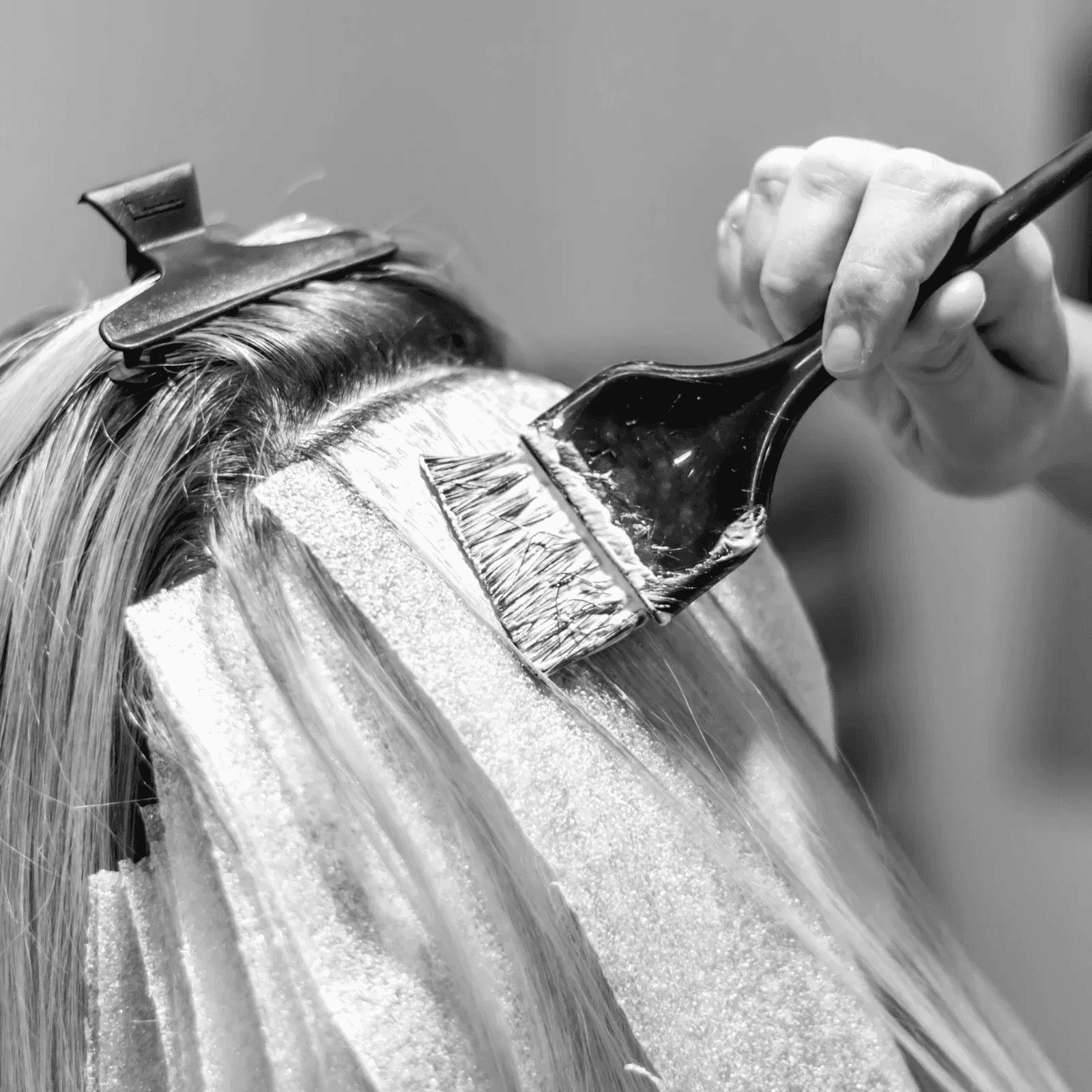 Hairdresser applying color to a client's hair with a brush on foil strips.