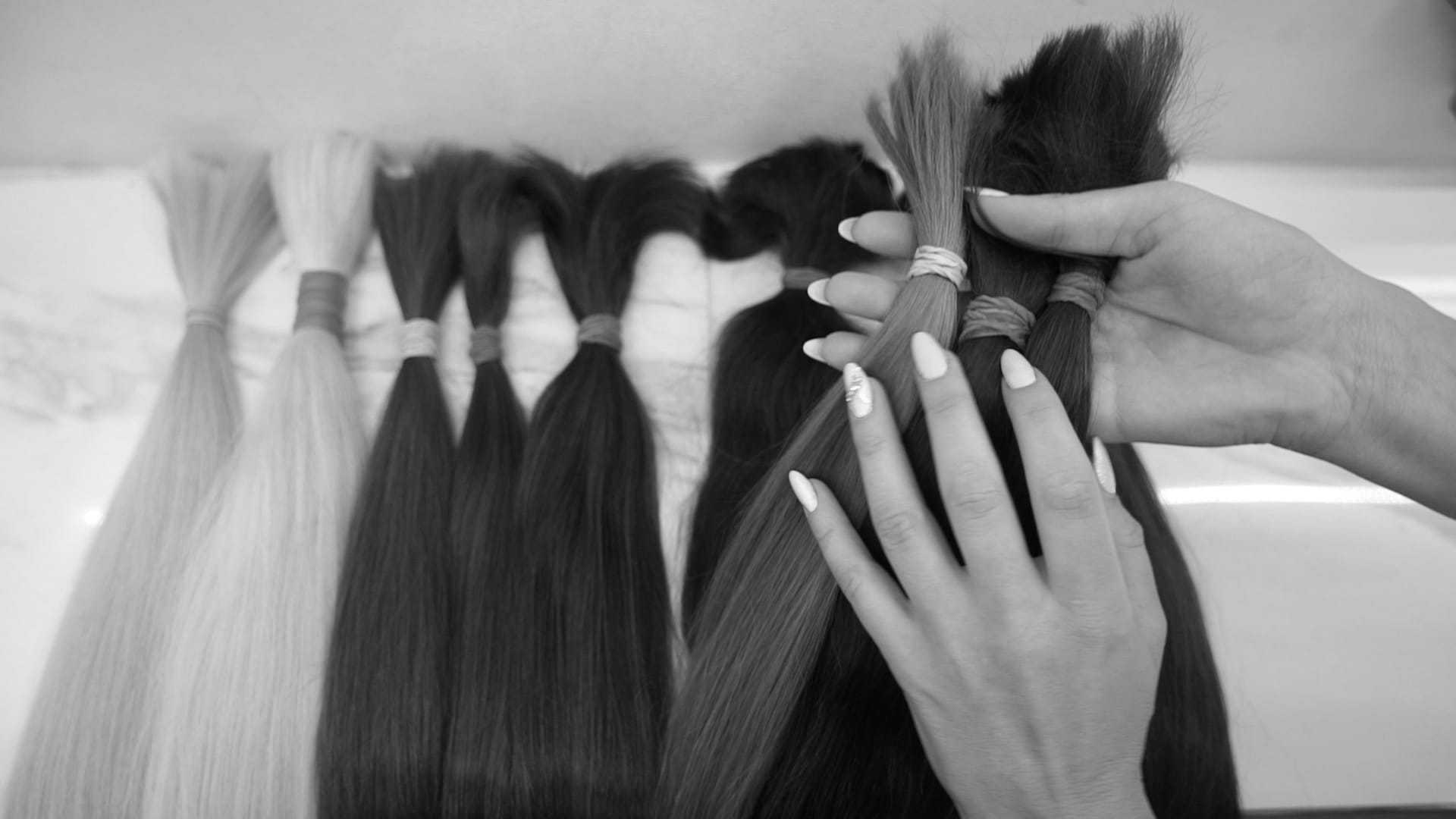 Hands selecting bundles of hair extensions in various shades and textures.