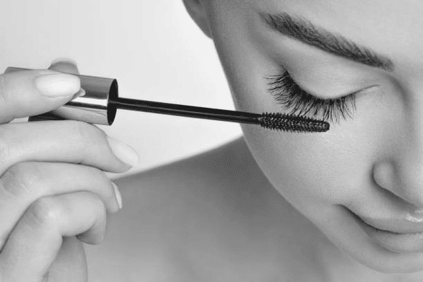 Woman applying mascara to eyelashes with a gentle smile.