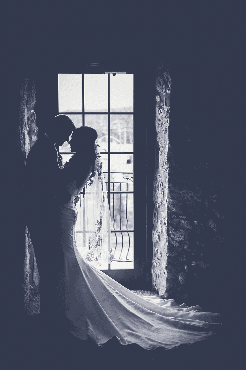 Bride and groom sharing a romantic moment by a window in silhouette.
