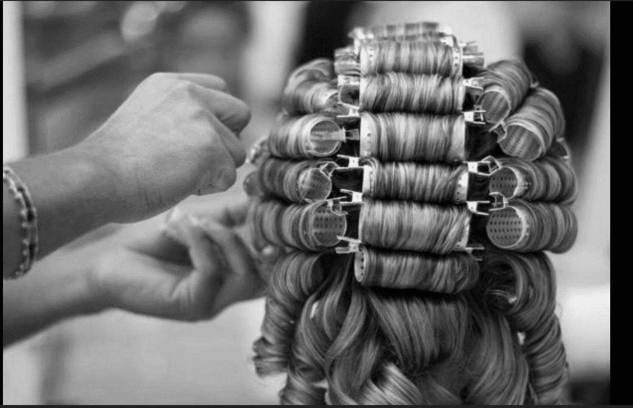 Hair stylist setting curls with rollers in a salon.